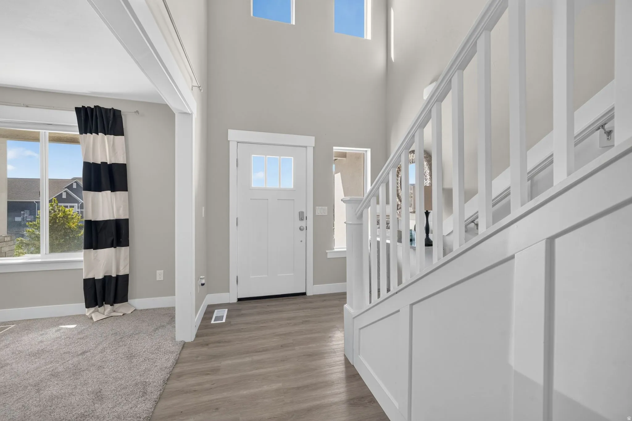 Two-story entryway featuring wood-finish flooring, a white paneled staircase, and a transom window above the front door