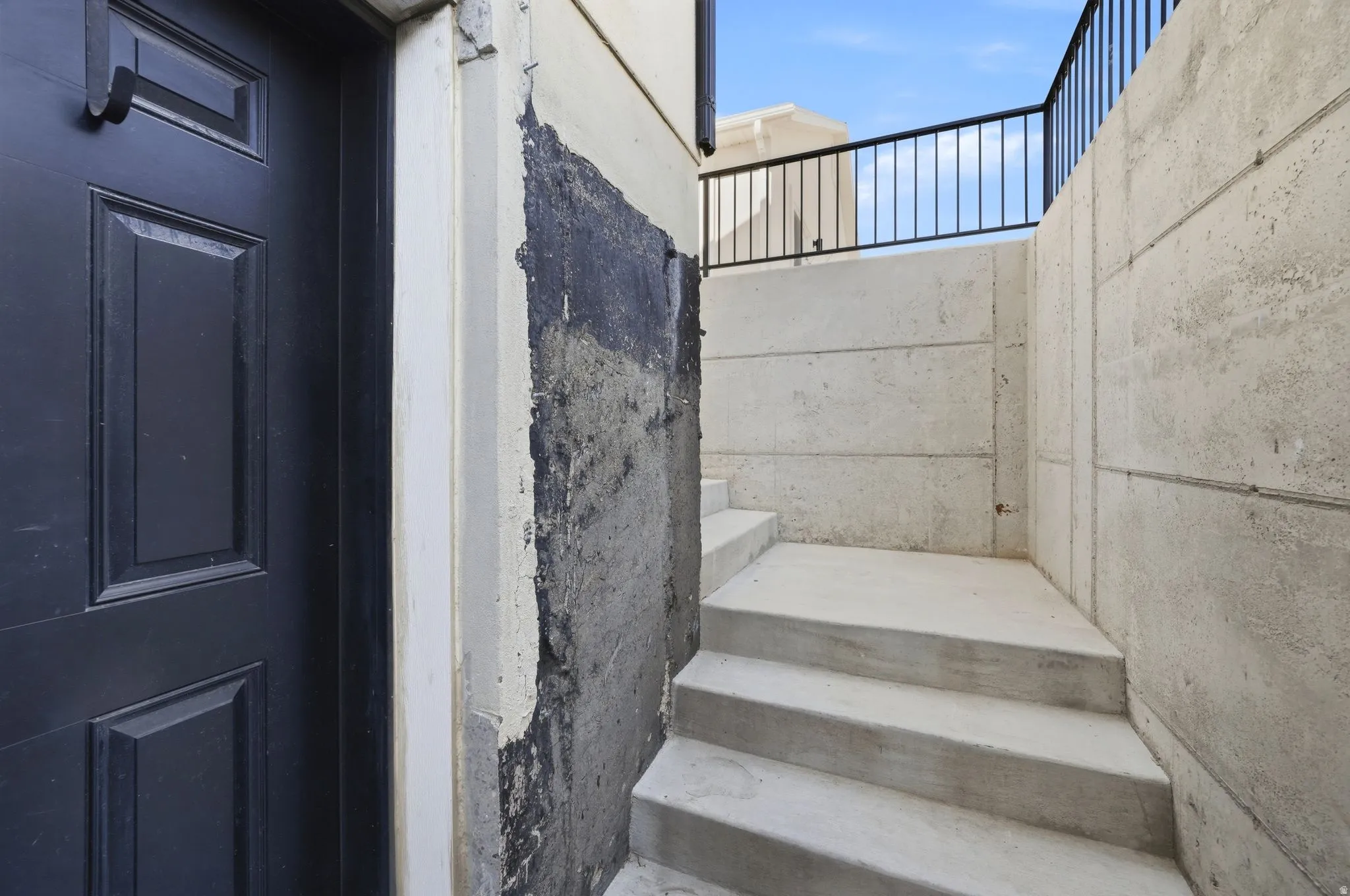 Recessed entry featuring a paneled door, concrete steps, and a black metal railing