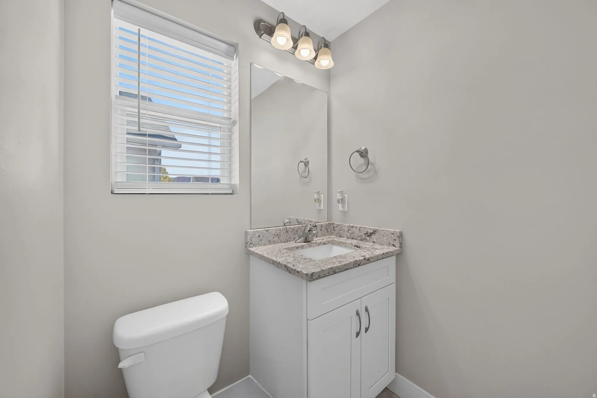 White vanity with a stone-finish countertop and an undermount sink