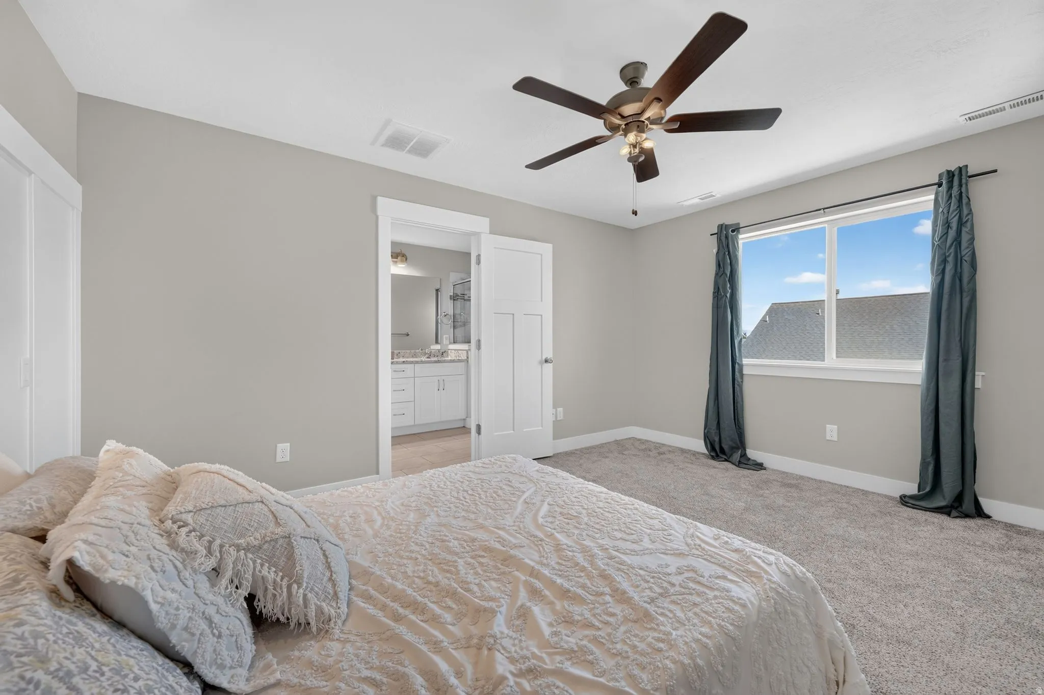 Plush carpeting throughout, a ceiling fan with integrated lighting, and a large window providing ample natural light