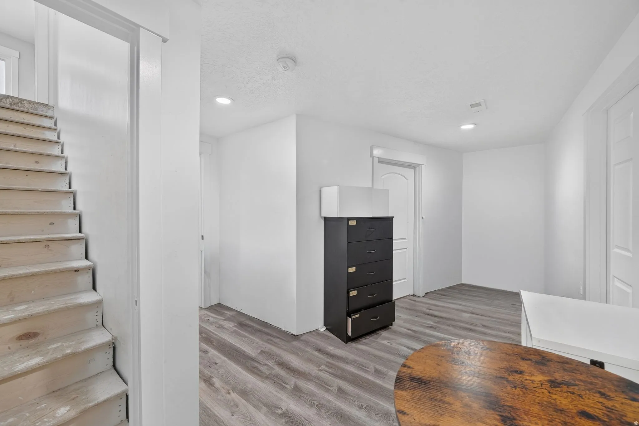 Wood-finish flooring throughout, bright white walls, and recessed ceiling lighting