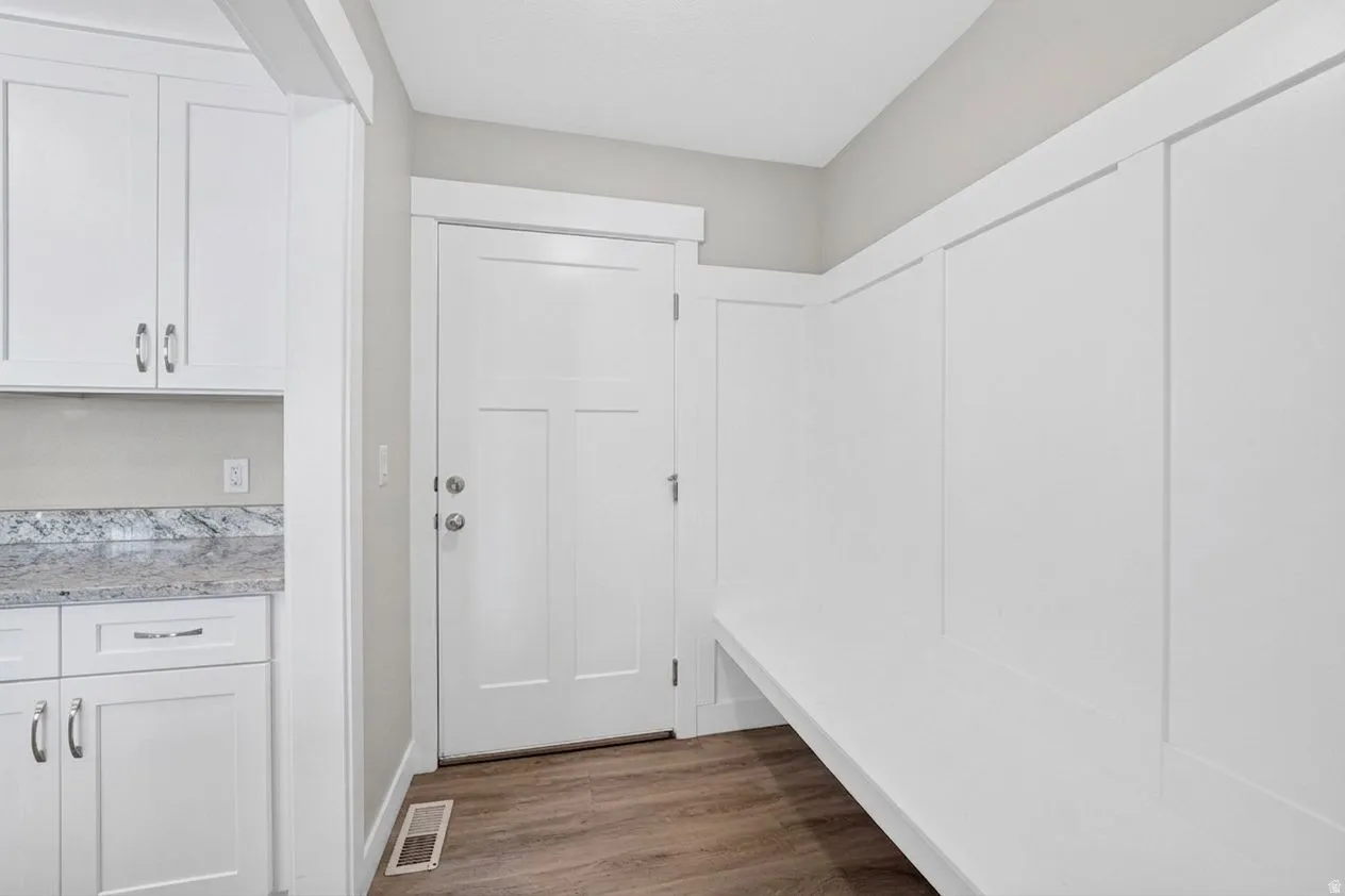 Built-in white cabinetry with chrome hardware, speckled countertop, and wood-finish flooring