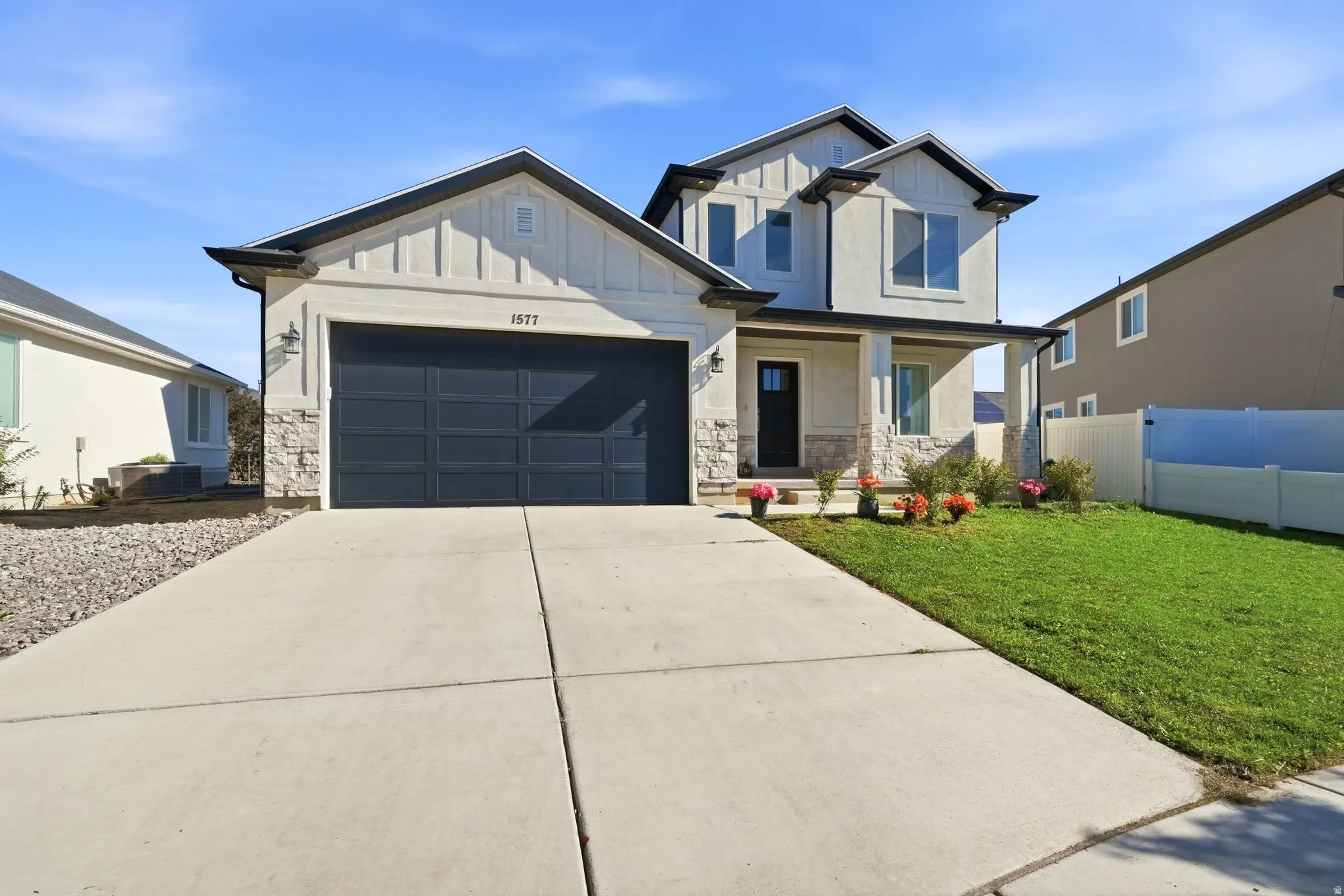 Contemporary two-story residence featuring a gray paneled garage door, stone and stucco exterior, and a covered front entry