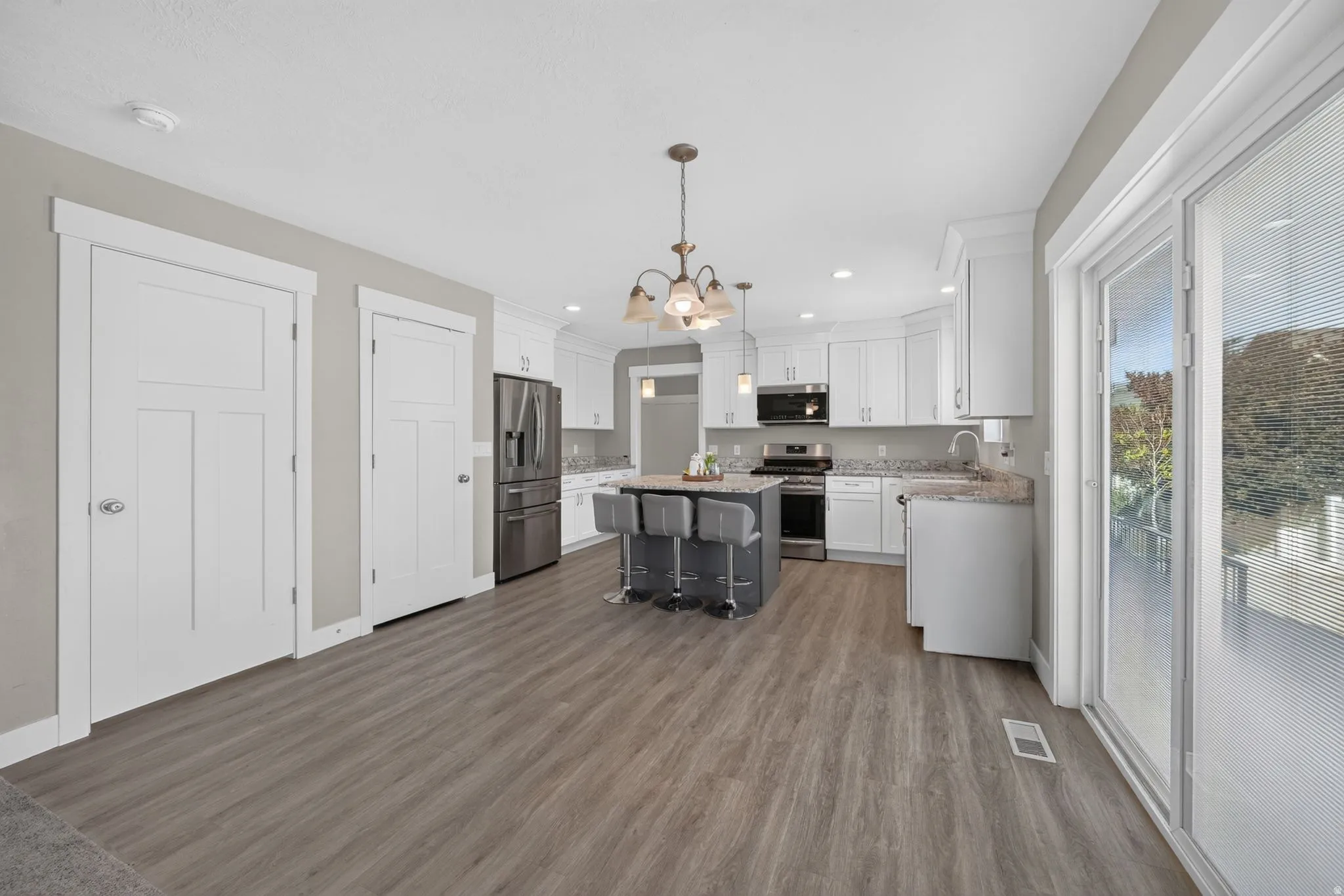Modern kitchen featuring white cabinetry, stainless steel appliances, a dark-toned island with seating, wood-finish flooring, and sliding glass doors