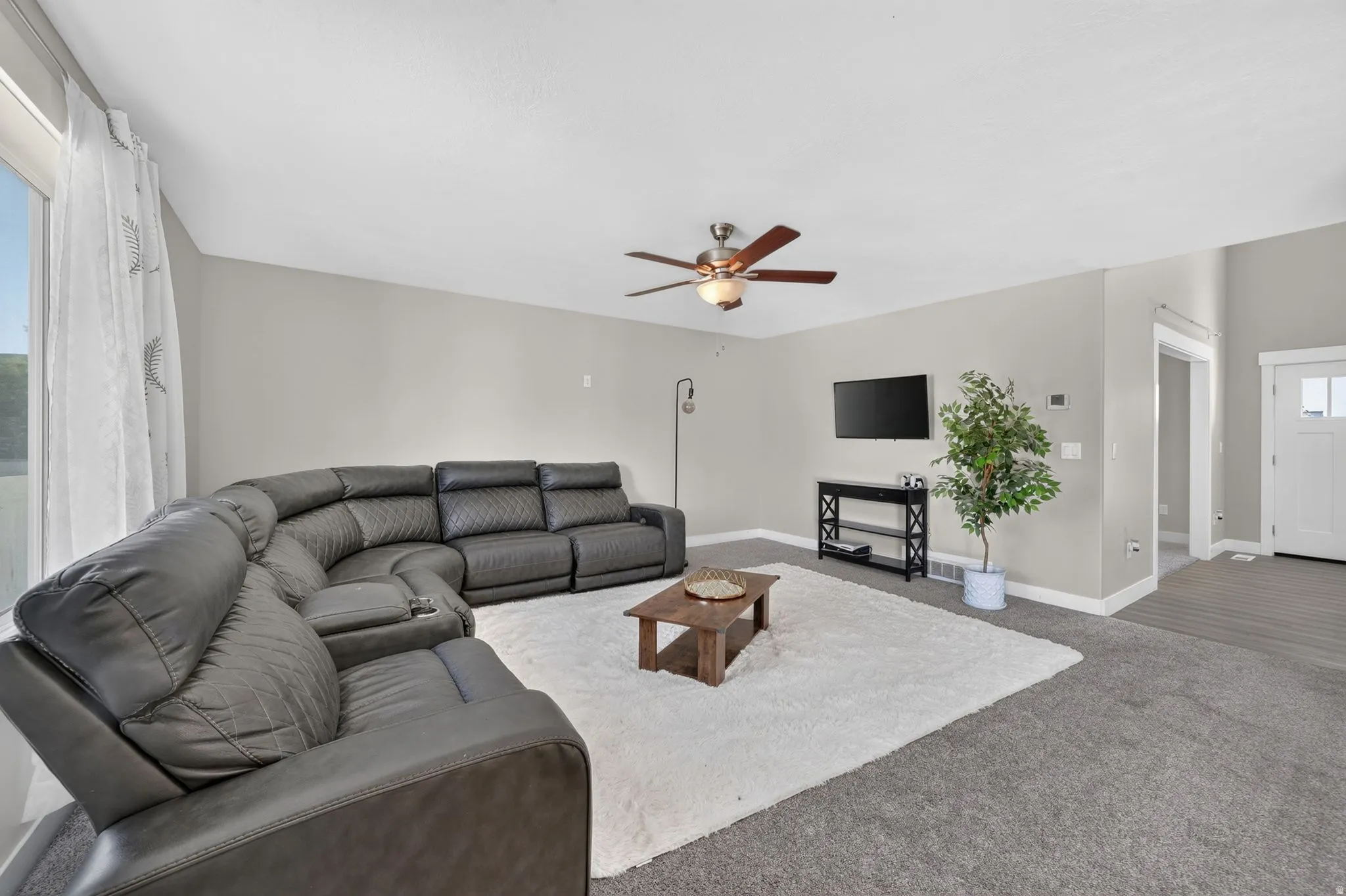 Recessed lighting, ceiling fan with integrated lighting, wall-mounted television, and a white paneled entry door