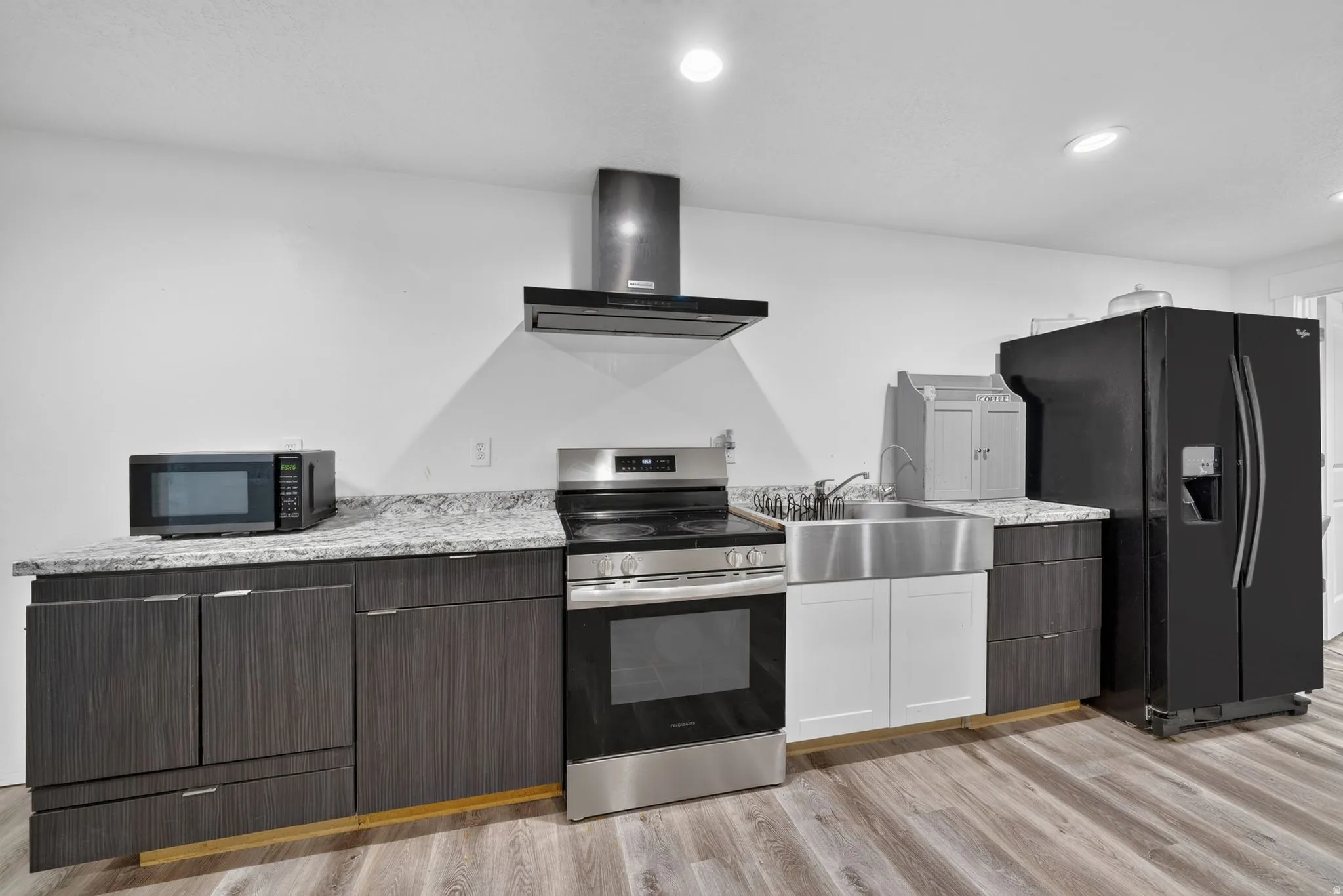 Contemporary kitchen featuring a stainless steel range with overhead ventilation, a farmhouse-style sink, and wood-finish flooring