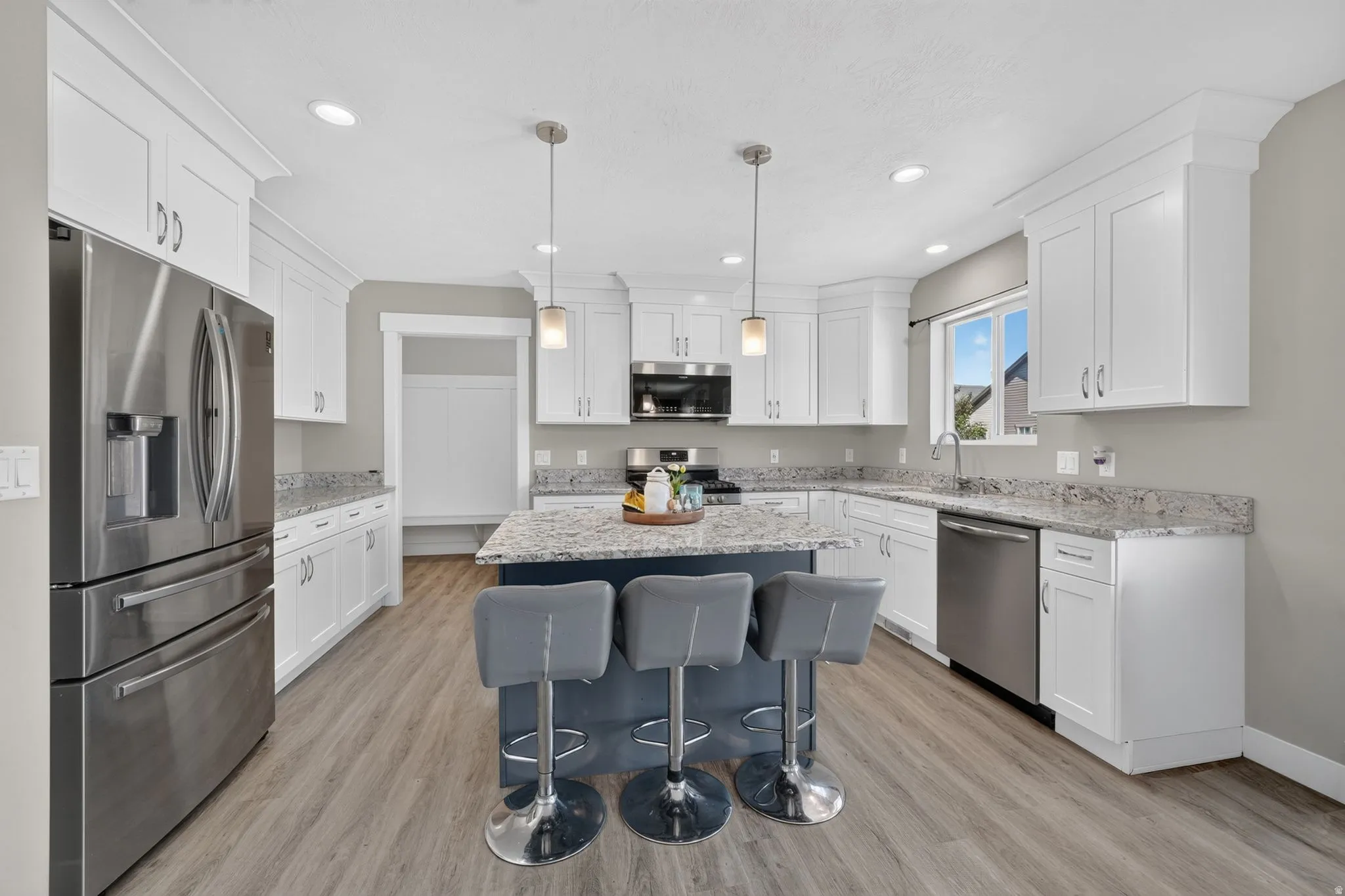 Spacious kitchen featuring white cabinetry, granite countertops, wood-finish flooring, stainless steel appliances, and a central island with pendant lighting
