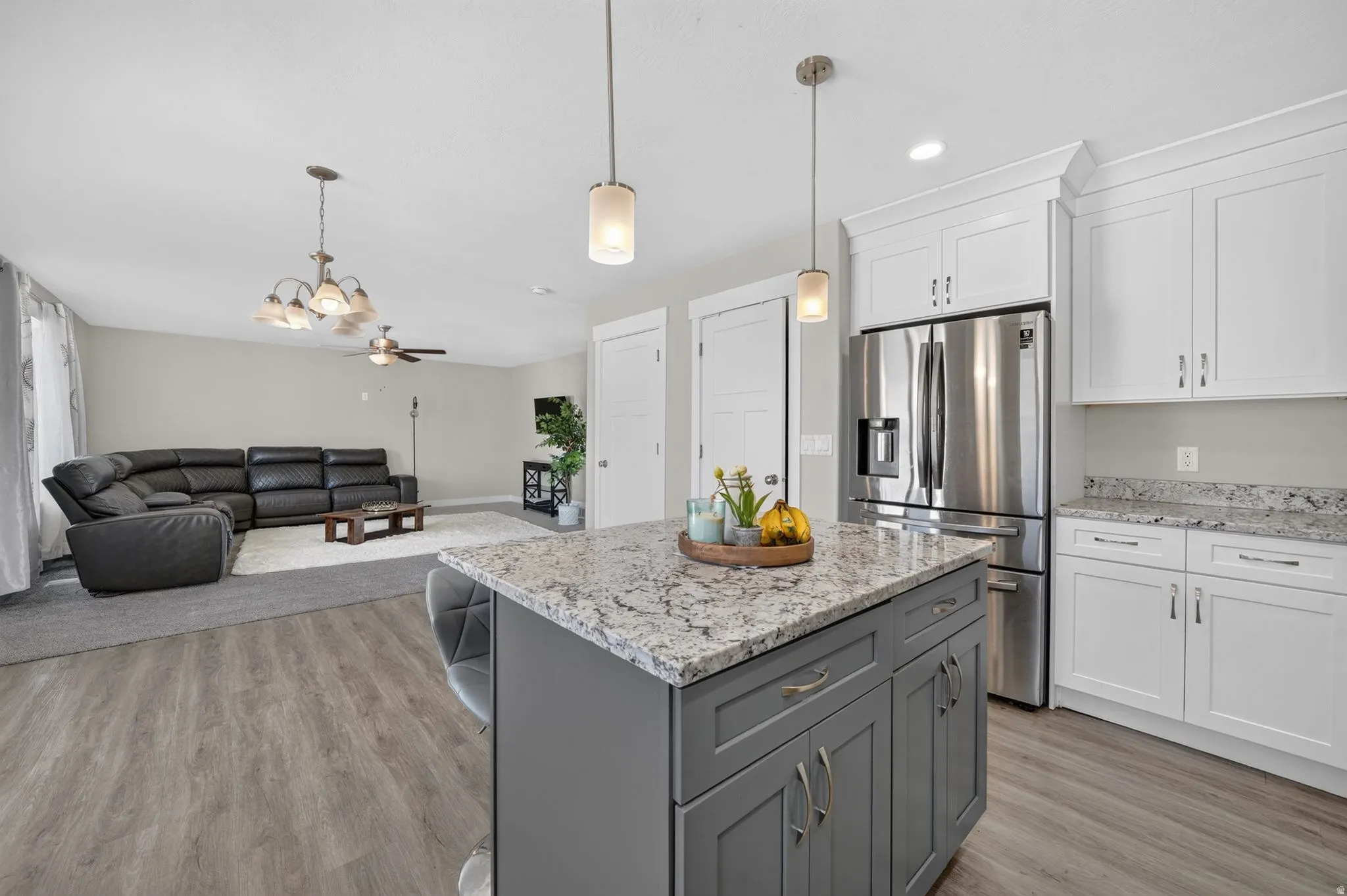 Kitchen island with a light-toned countertop, pendant lighting, stainless steel refrigerator, white cabinetry, and wood-finish flooring