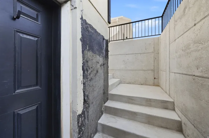 Recessed entry featuring a paneled door, concrete steps, and a black metal railing