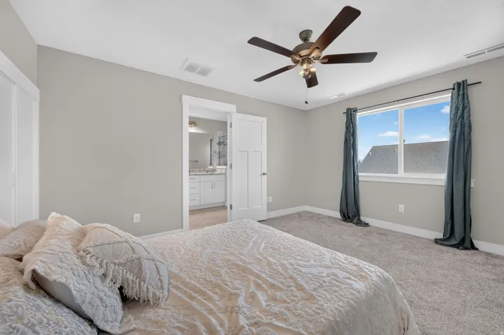 Plush carpeting throughout, a ceiling fan with integrated lighting, and a large window providing ample natural light