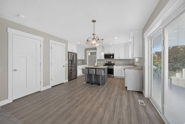 Modern kitchen featuring white cabinetry, stainless steel appliances, a dark-toned island with seating, wood-finish flooring, and sliding glass doors