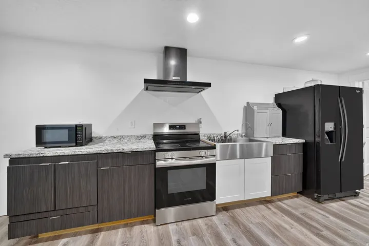 Contemporary kitchen featuring a stainless steel range with overhead ventilation, a farmhouse-style sink, and wood-finish flooring