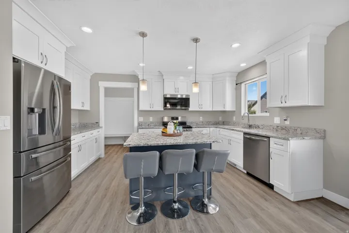 Spacious kitchen featuring white cabinetry, granite countertops, wood-finish flooring, stainless steel appliances, and a central island with pendant lighting