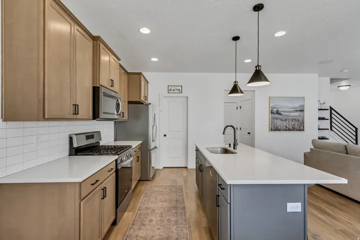 Kitchen featuring stainless steel appliances, light wood-finish cabinetry, white subway tile backsplash, and a large island with a sink