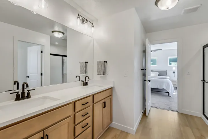 Dual vanity with integrated sinks, light-toned wood-finish cabinetry, matte black hardware, and light wood-finish flooring