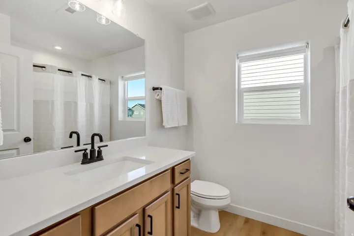 Bathroom featuring a wood-finish vanity with a single basin sink, white countertop, and matte black fixtures