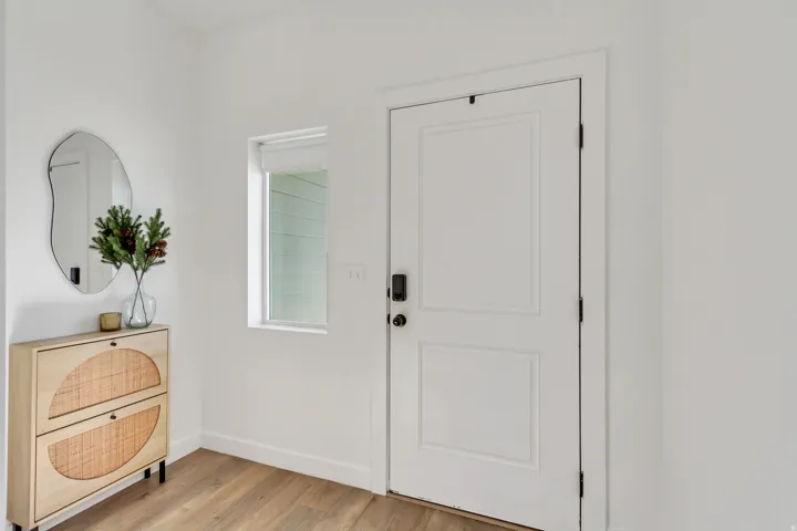 Wood-finish flooring, white walls, and a white paneled entry door with dark hardware
