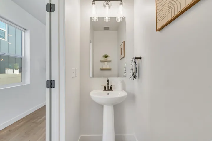 White pedestal sink with a dark bronze faucet, accompanied by a rectangular mirror and a three-bulb light fixture