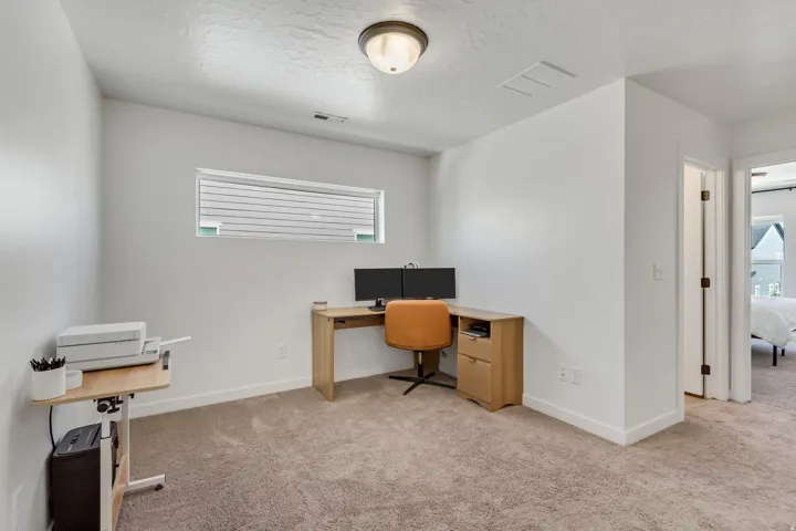 Carpeted flooring, white walls, horizontal window with blinds, overhead lighting fixture, and a doorway