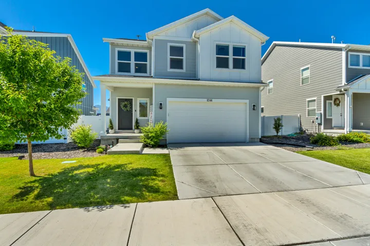 Two-story residence featuring light gray siding with white board and batten accents, an attached two-car garage, and a covered front porch with white columns