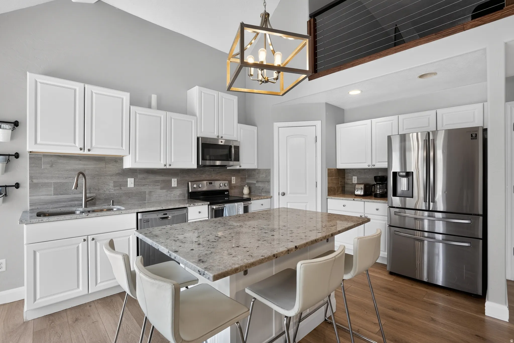 Kitchen featuring a center island with stone countertop, white cabinetry, stainless steel appliances, and wood-finish flooring