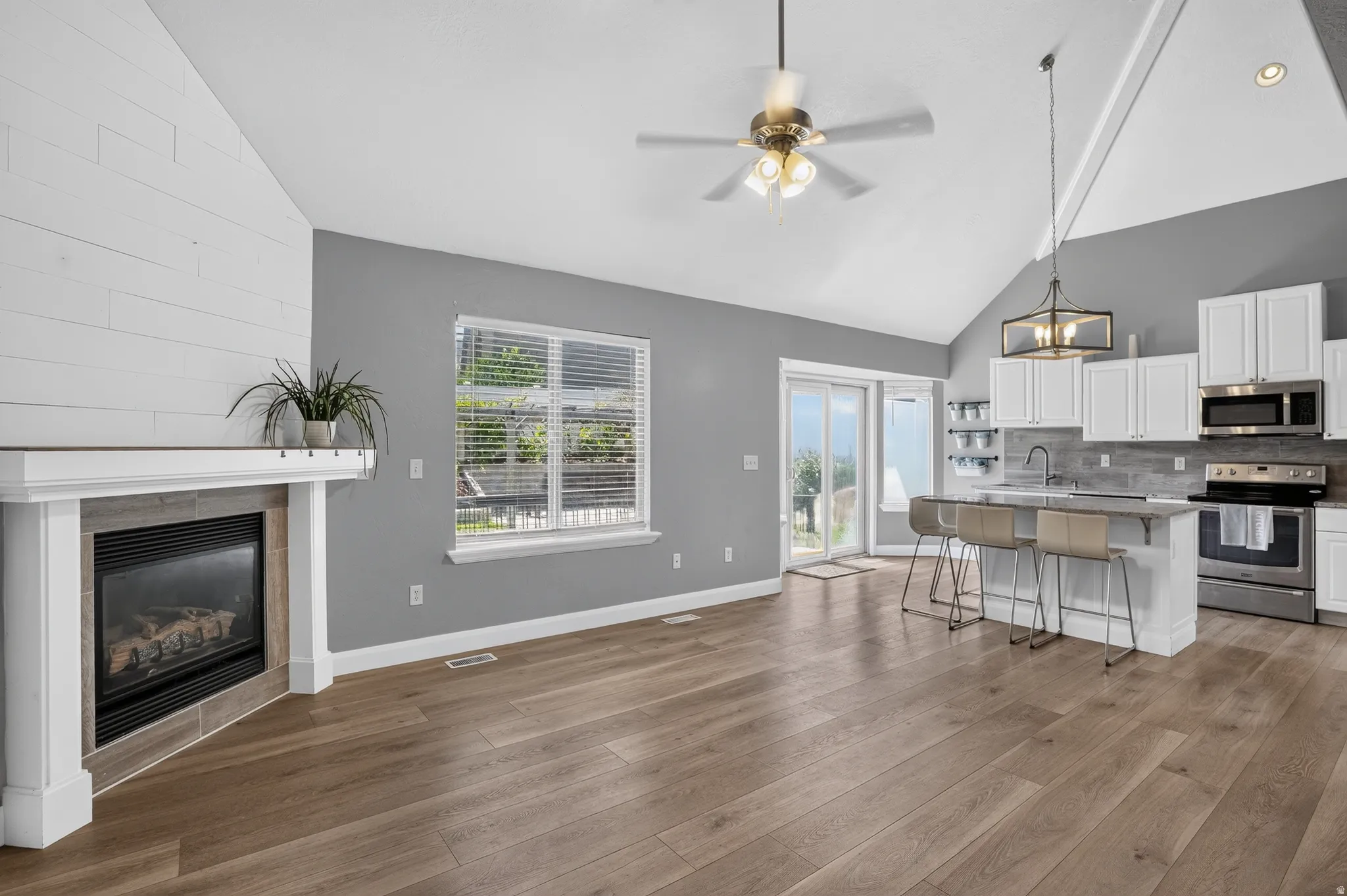 Open-concept living area featuring wood-finish flooring, a vaulted ceiling, and a fireplace with a shiplap accent wall