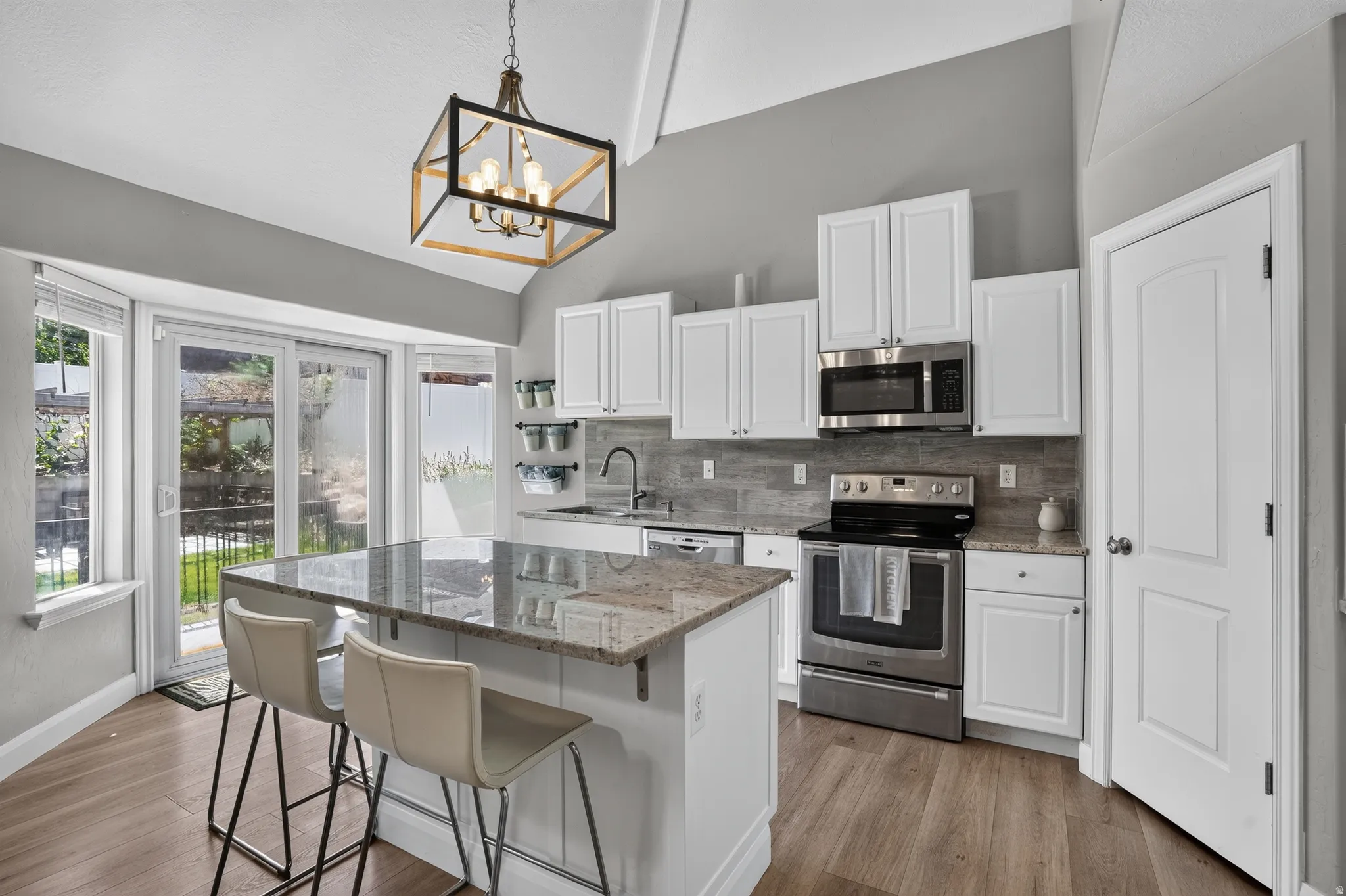 Kitchen featuring a spacious island with a stone countertop, white cabinetry, stainless steel appliances, and wood-finish flooring