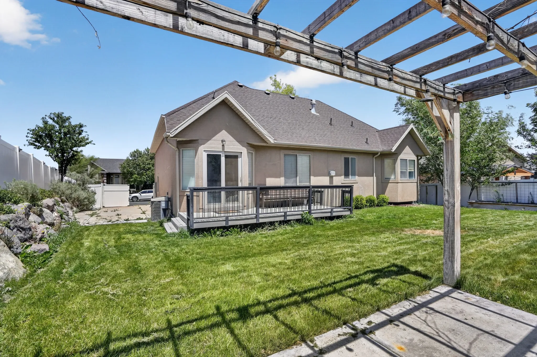 Expansive backyard featuring a pergola, manicured lawn, and a deck with dark railings