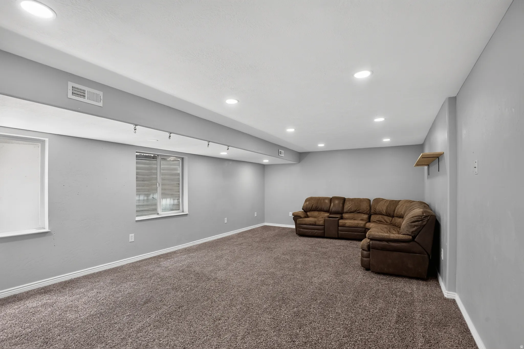 Spacious room featuring neutral gray walls, recessed ceiling lighting, textured brown carpeting, and white baseboards