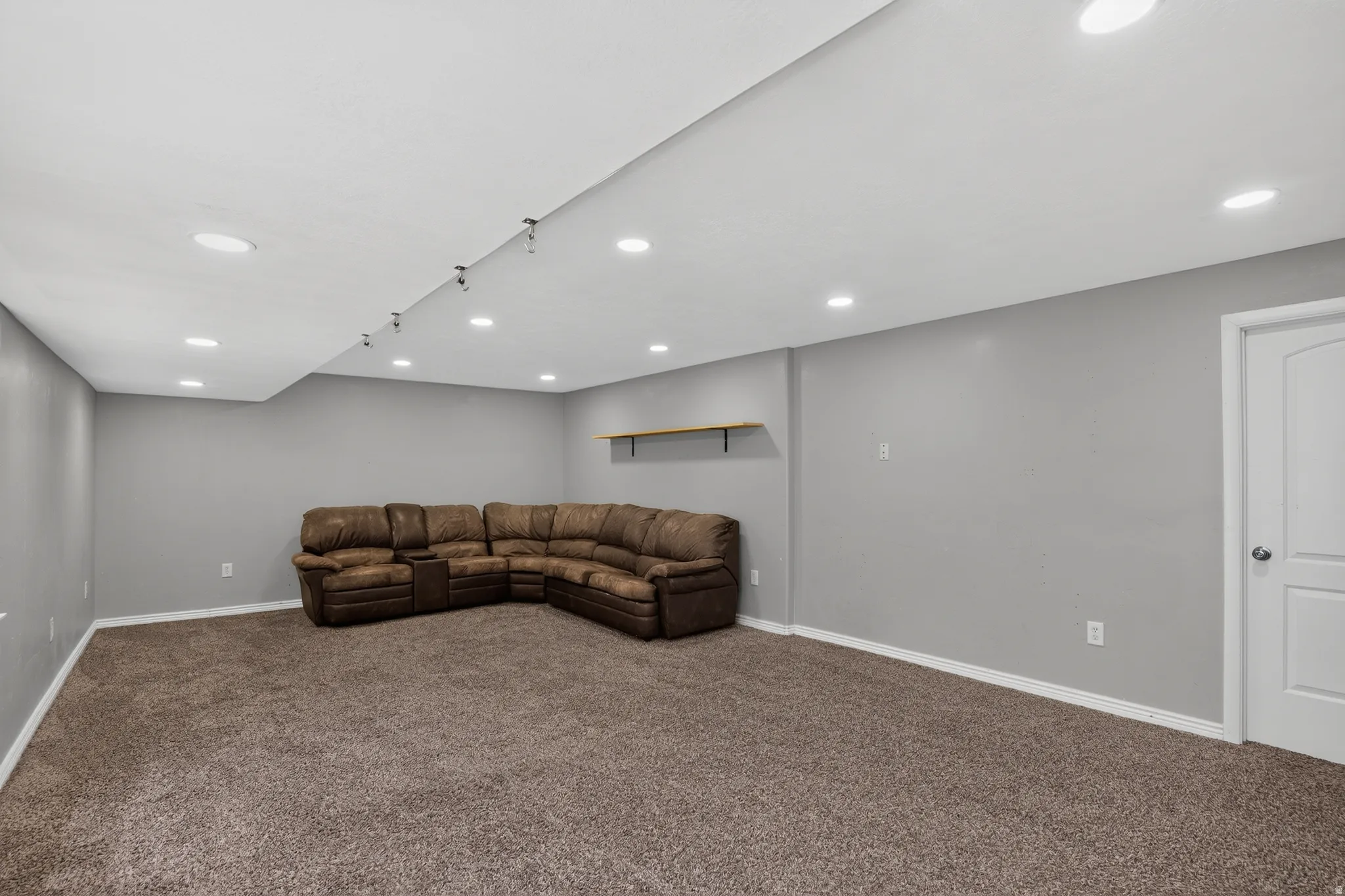 Spacious carpeted room featuring recessed lighting, a dropped ceiling detail with track lighting, light gray walls, white trim, and a white interior door