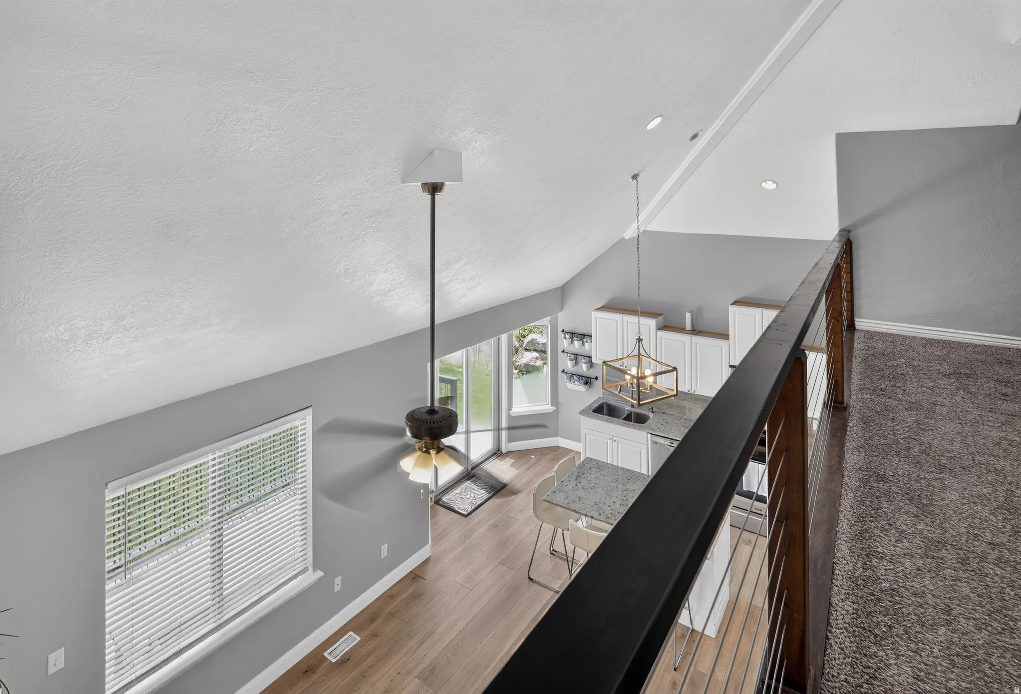 Open-concept living space with vaulted ceilings, wood-finish flooring, and a contemporary kitchen featuring white cabinetry and light-toned countertops
