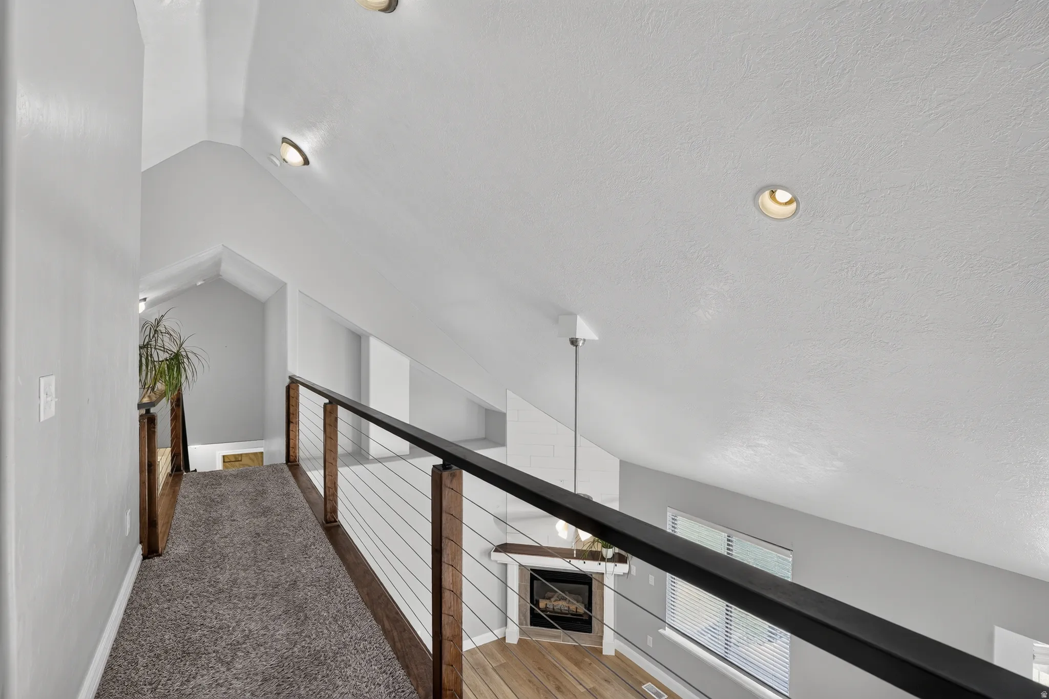 Upper-level hallway featuring a cable railing system, recessed lighting, and vaulted ceilings