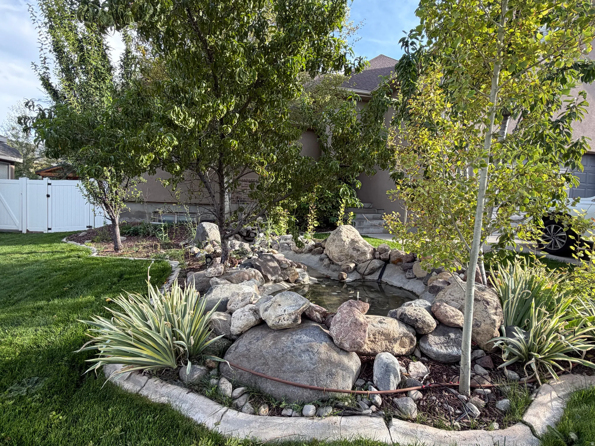 Pond feature with natural rock surround, established trees, perimeter landscaping, and manicured lawn