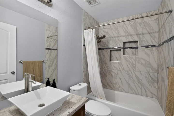 Full bathroom featuring a vessel sink, stone countertop, tub with shower, and tile surround with decorative accent band and integrated niches