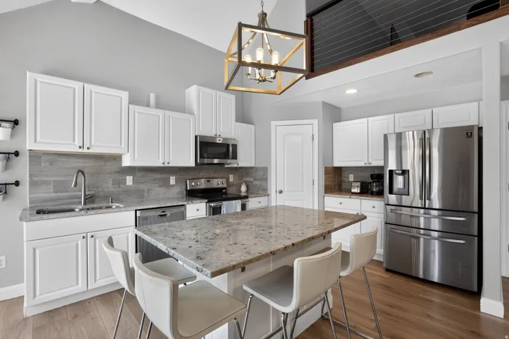 Kitchen featuring a center island with stone countertop, white cabinetry, stainless steel appliances, and wood-finish flooring