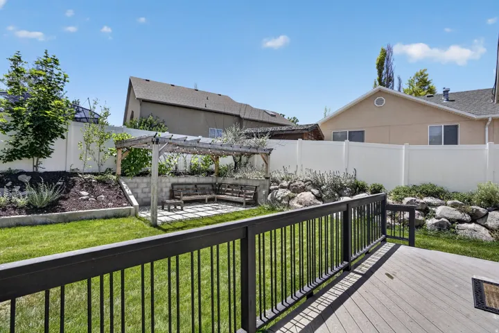 Expansive backyard featuring a composite deck with black metal railing, a manicured lawn, a terraced landscape with natural rock elements, and a pergola-covered patio area with built-in seating
