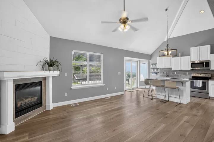 Open-concept living area featuring wood-finish flooring, a vaulted ceiling, and a fireplace with a shiplap accent wall
