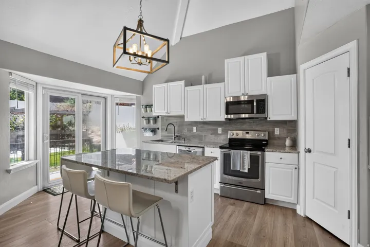 Kitchen featuring a spacious island with a stone countertop, white cabinetry, stainless steel appliances, and wood-finish flooring