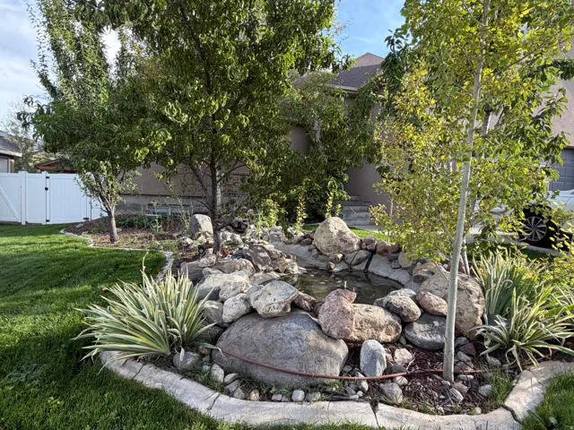 Pond feature with natural rock surround, established trees, perimeter landscaping, and manicured lawn
