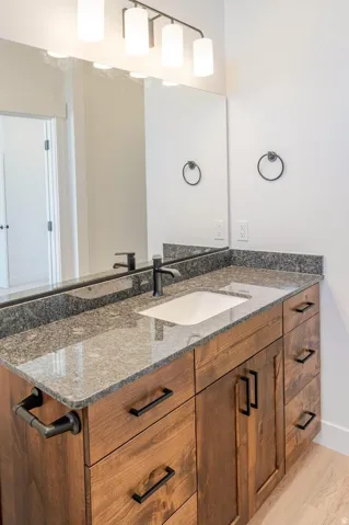 Wood-finish vanity with an undermount sink, a stone countertop, a matte black faucet, and a large mirror with integrated lighting