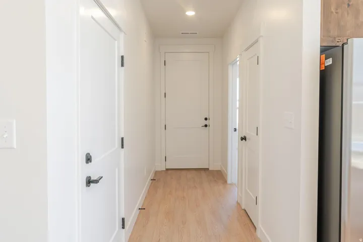 Light-toned wood-finish flooring, recessed ceiling lighting, and white paneled doors with dark hardware