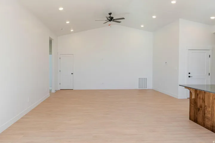Vaulted ceilings with recessed lighting, wood-finish flooring, a ceiling fan, and a wood-paneled island with a stone countertop