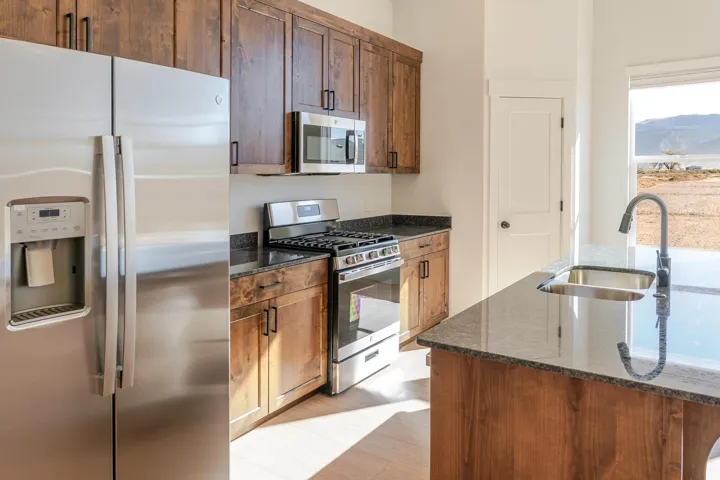 Stainless steel appliance suite, wood-finish cabinetry, dark stone countertops, island with undermount sink, and expansive exterior scenery