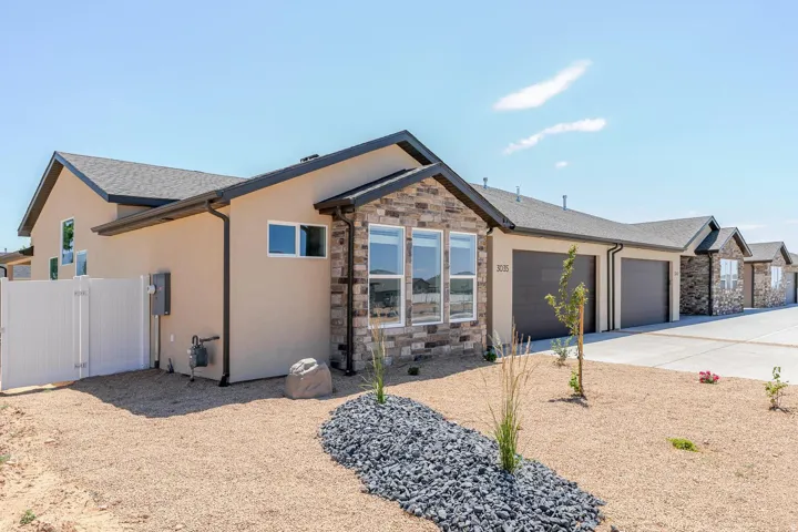Stucco and stone exterior, multi-pane windows, attached garages, gravel landscaping, and a white privacy fence
