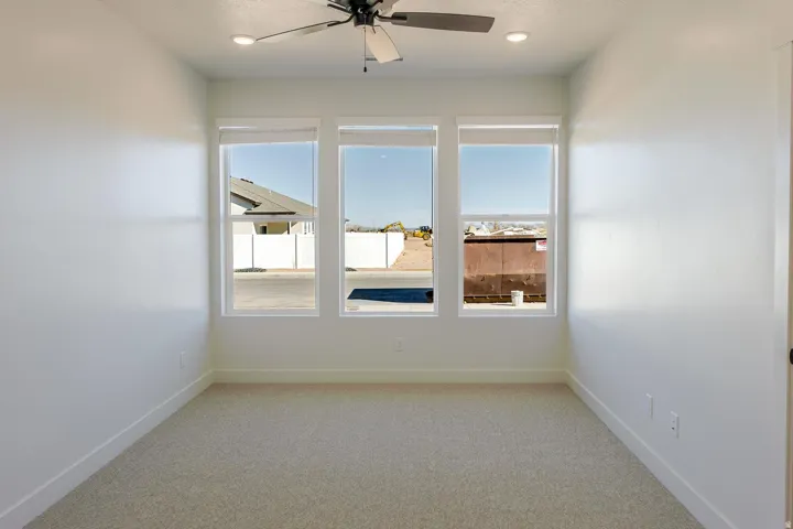 Neutral-toned carpeting, three expansive windows, recessed lighting, and a ceiling fan with integrated lighting