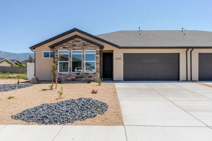 Stucco exterior with stone accent facade, prominent front-facing windows, attached multi-car garage, and a concrete driveway