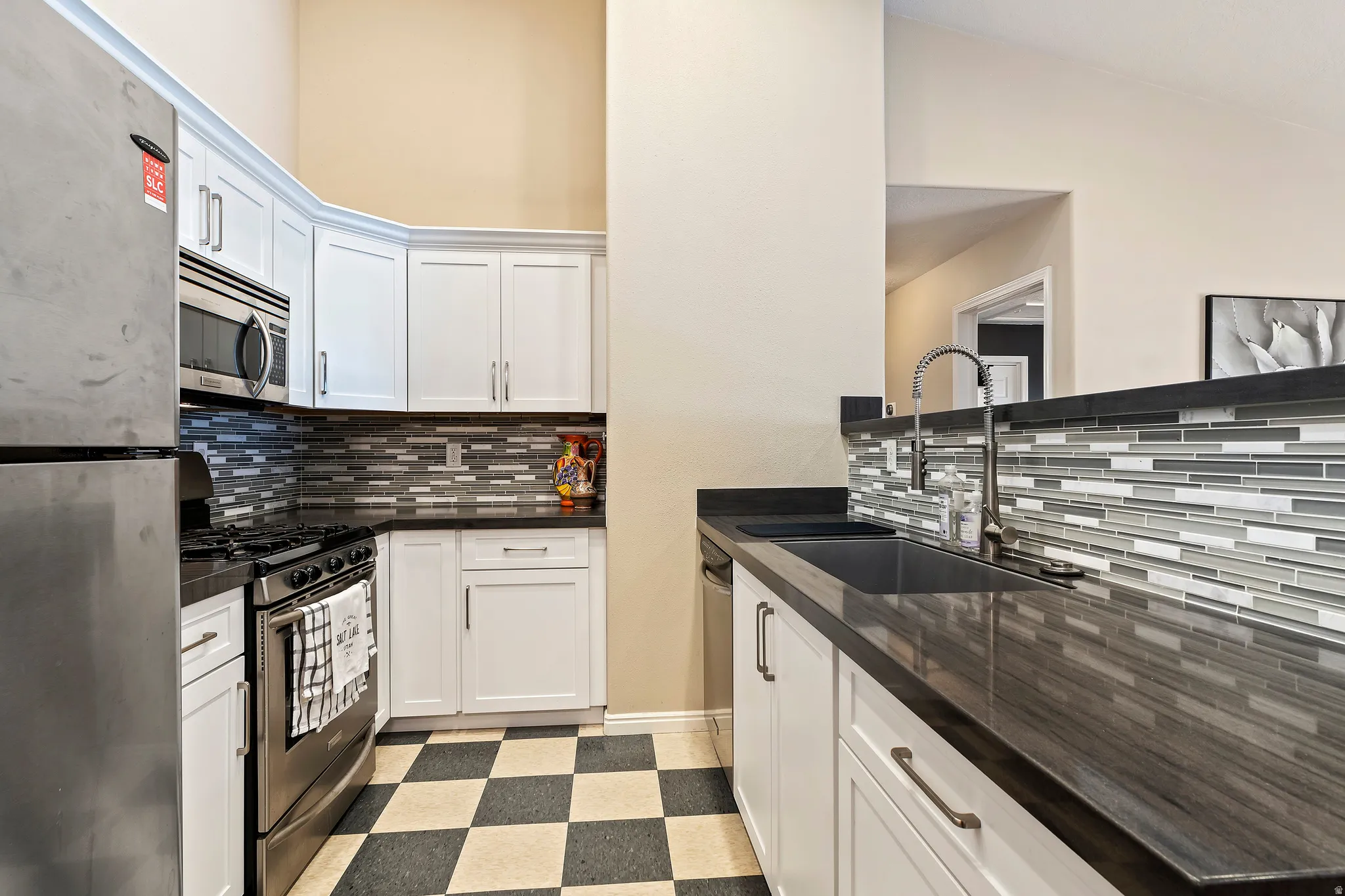 Kitchen featuring white cabinetry, dark countertops, a mosaic tile backsplash, and checkerboard floor tiles