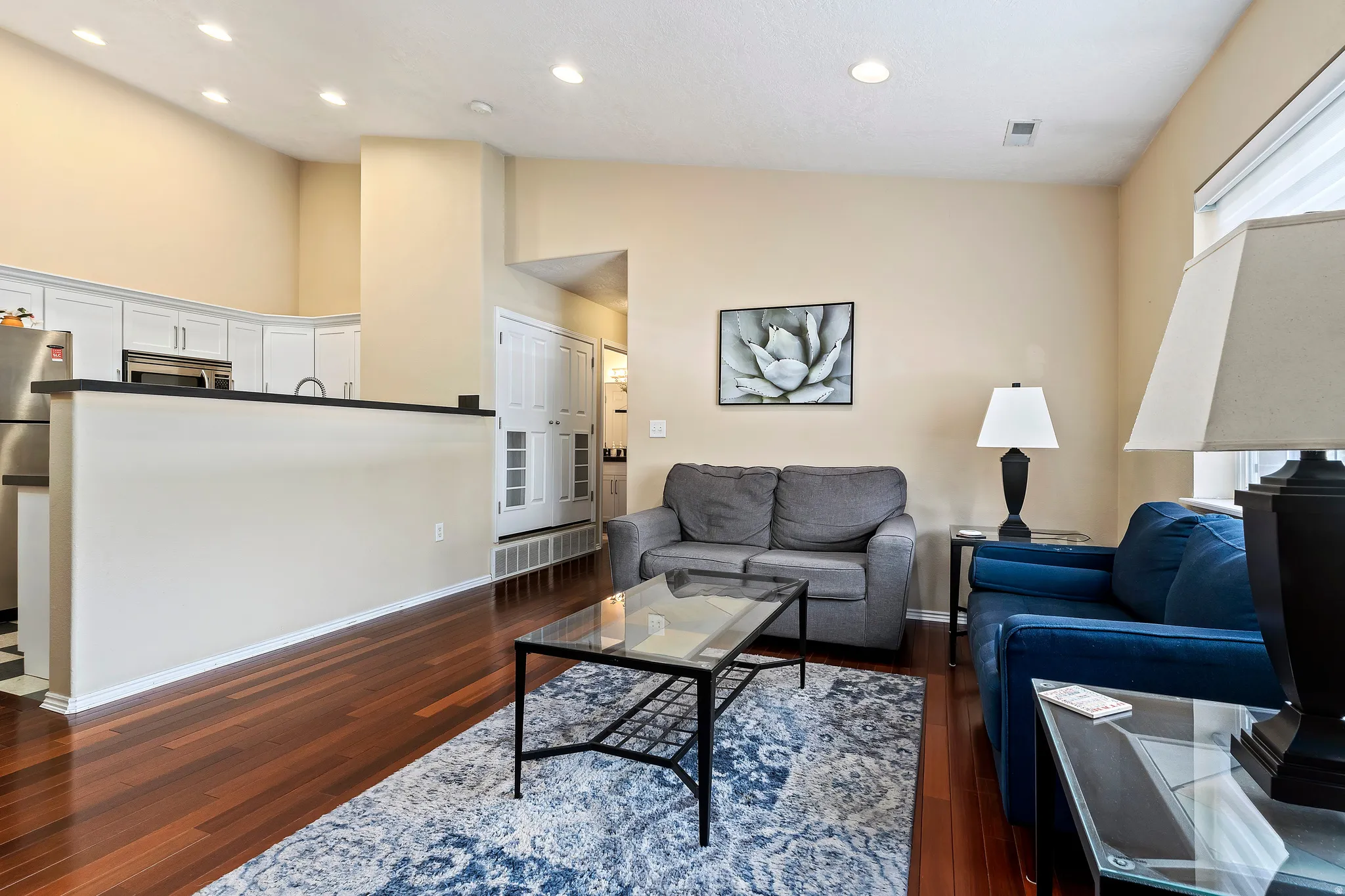 Vaulted ceilings, wood-finish flooring, recessed lighting, and kitchen with white cabinetry and stainless steel appliances