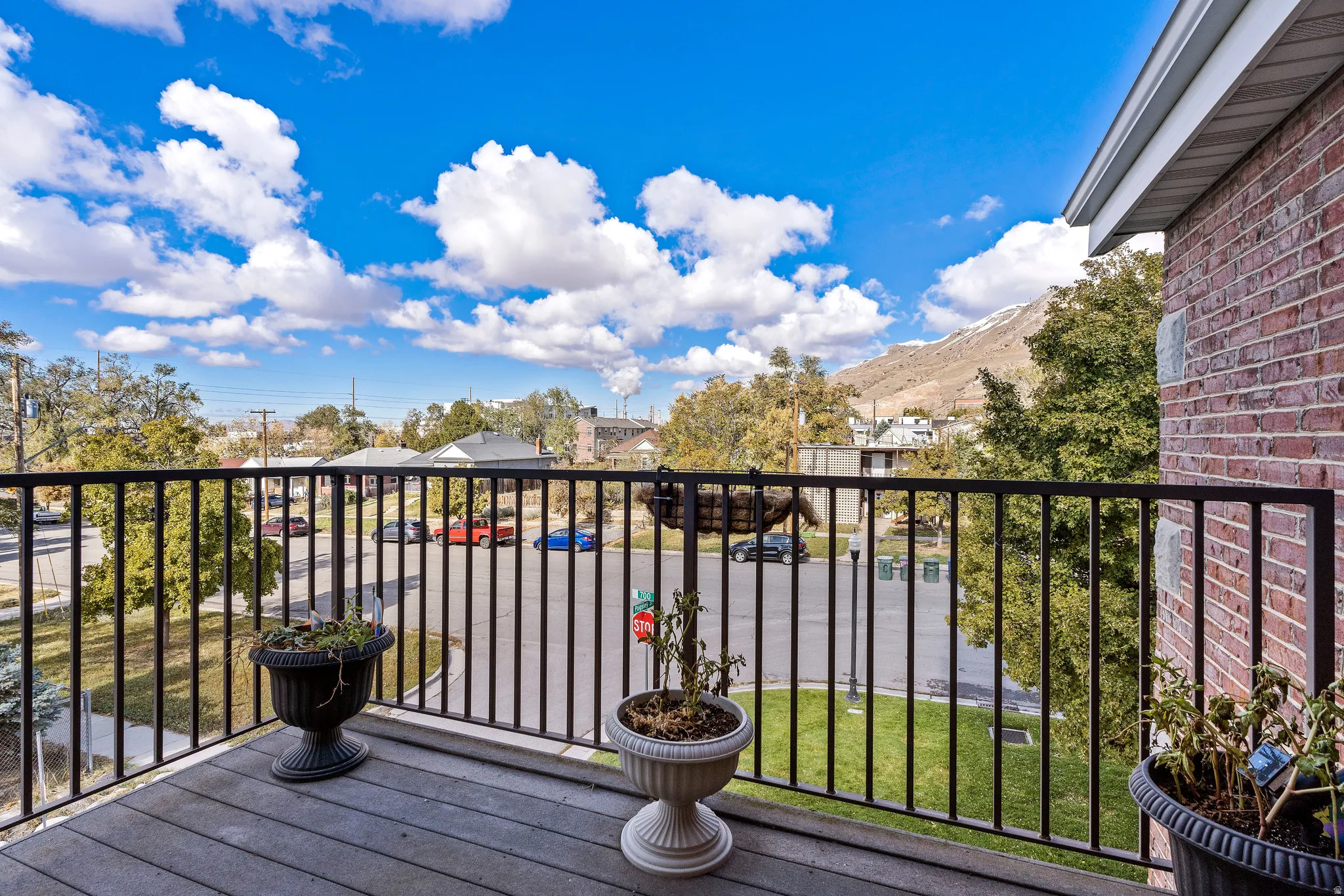 Balcony featuring wood-finish decking, black metal railing, and brick exterior wall