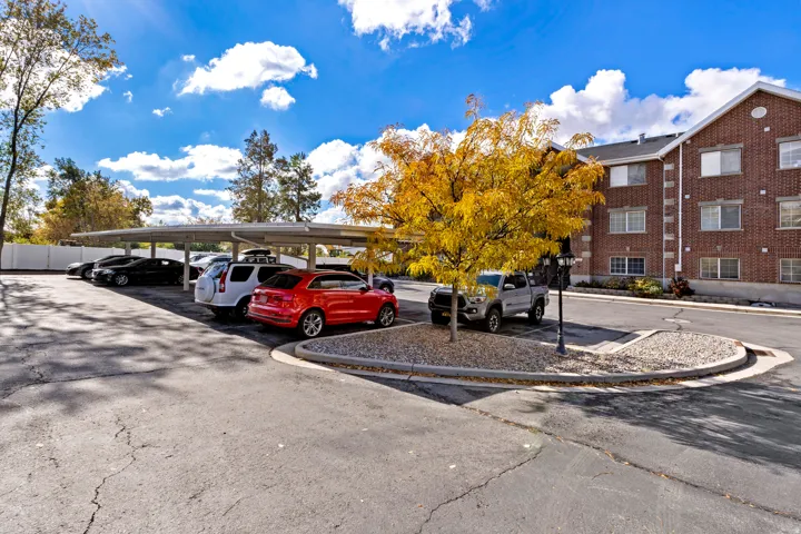 Covered parking structure, asphalt paved lot, brick building exterior, multiple windows, and a planted tree